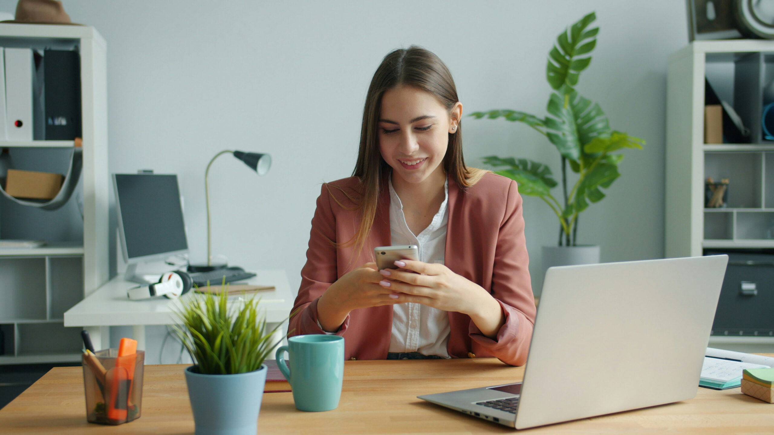 Woman sitting at a desk with an open laptop while looking at her phone.