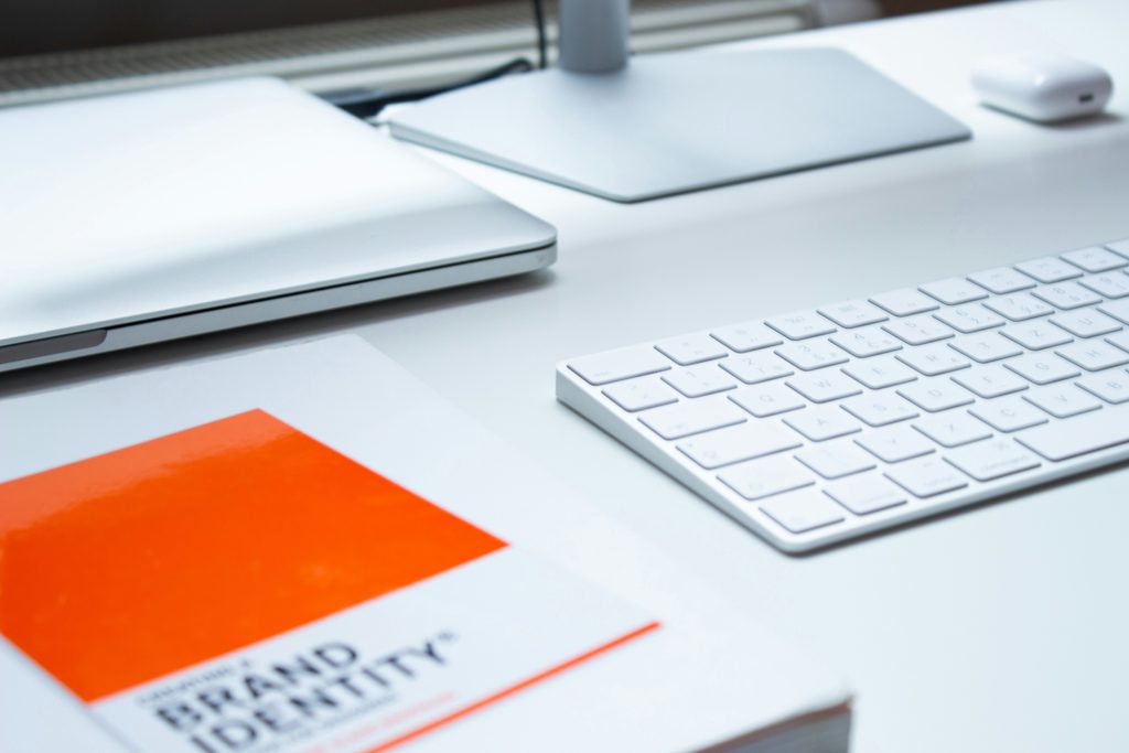 Desk with keyboard, monitor, book on brand identity, and a notebook